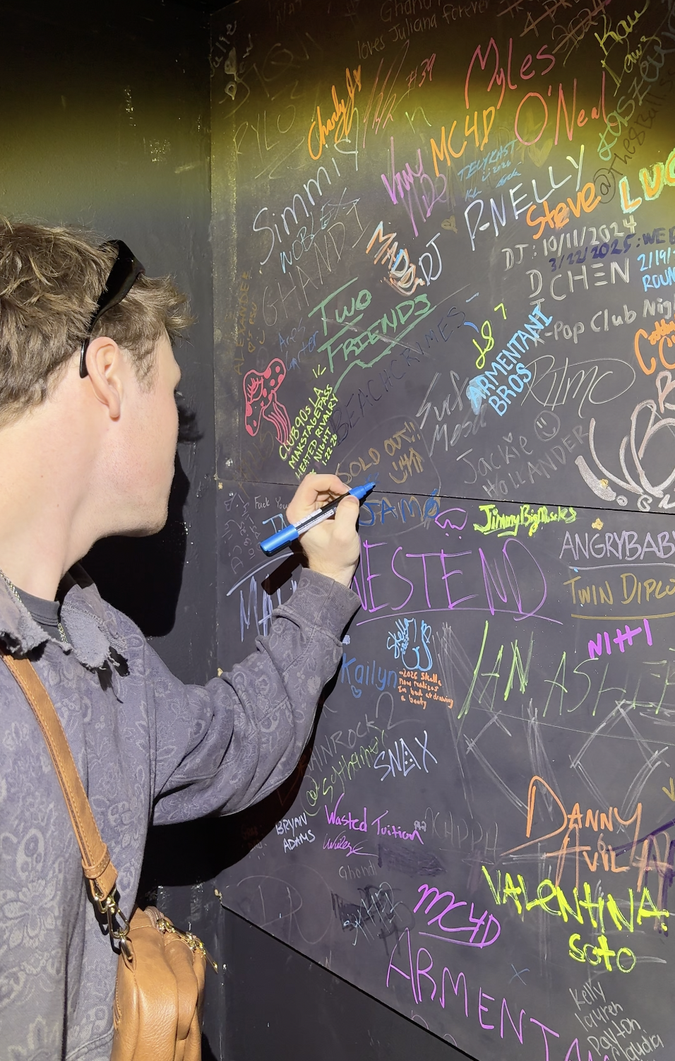 JAMØ signs his name on the artist wall at Stage West, adding his signature alongside Westend, Mau P, and other artists who have previously performed at the venue.
